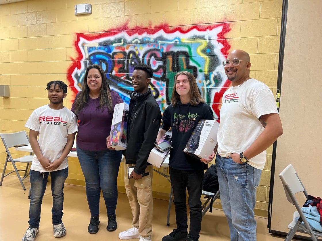 Four young people and one man in front of yellow wall with multicolored artwork.