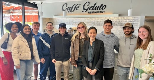 A group of nine people stand together smiling inside Caffé Gelato Restaurant, posing for a group photo in front of the counter.