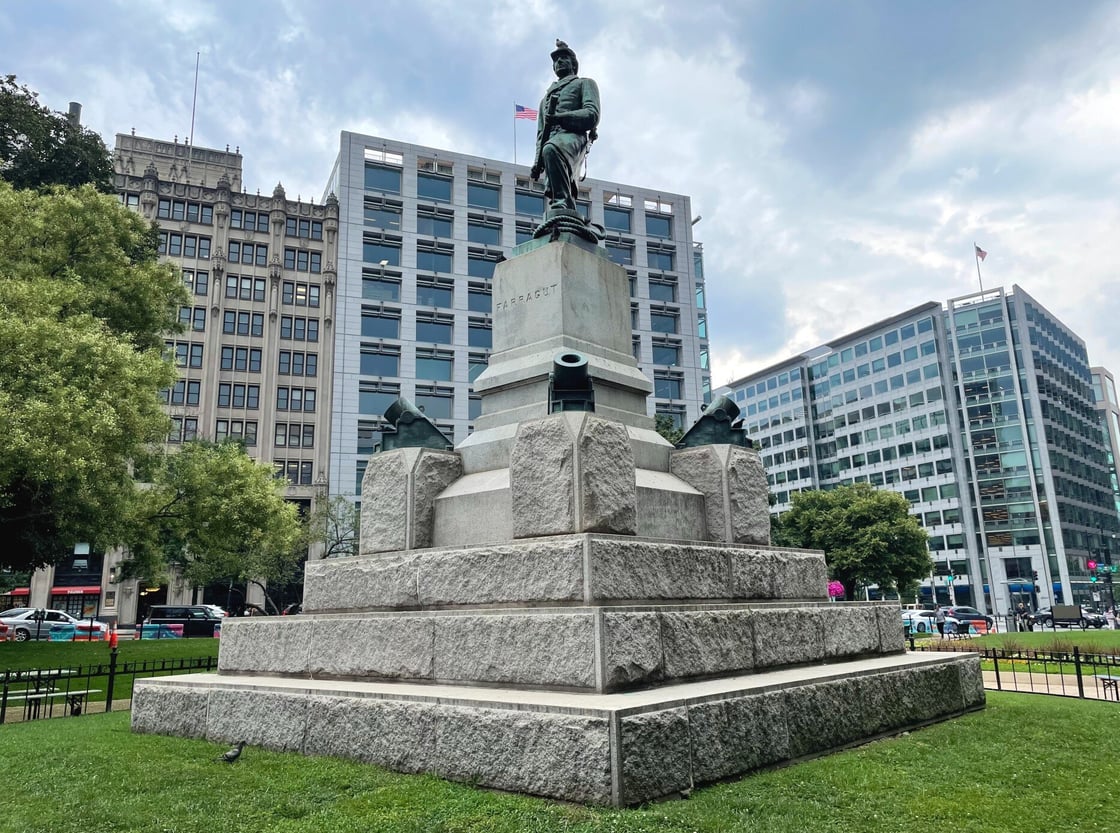 Green statue of warrior on stone bust with green cannons, grey stand and grey stone steps 