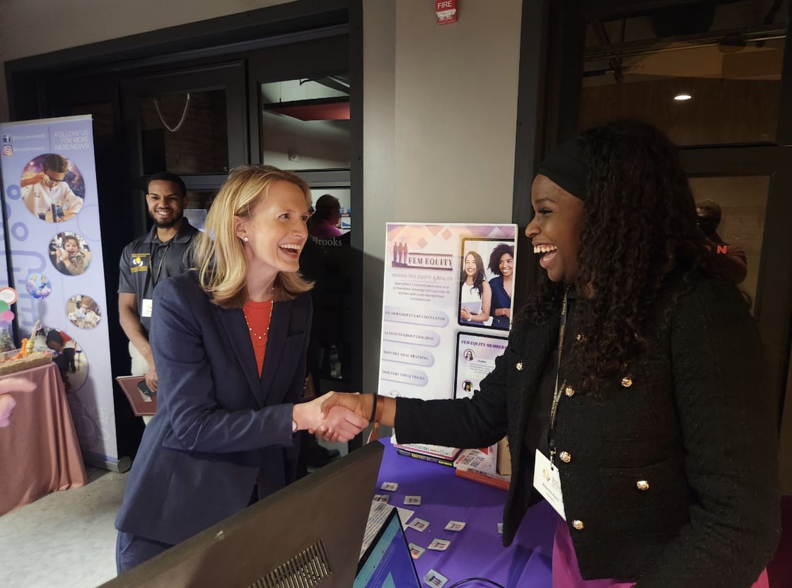Two women shaking hands over table with purple tablecloth
