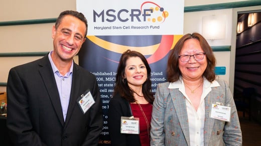 Three people smiling in front of a Maryland Stem Cell Research Fund banner at an event.