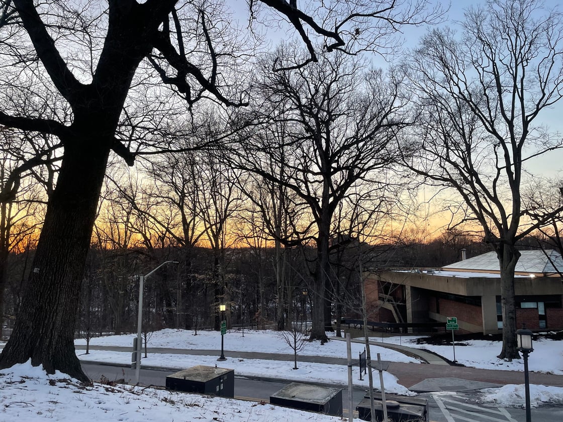 An orange sunset hangs behind a snow-covered college campus with dark trees