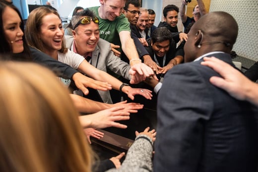 A group of diverse people in business attire, reaching their hands into the center of the group in a gesture of teamwork and unity.