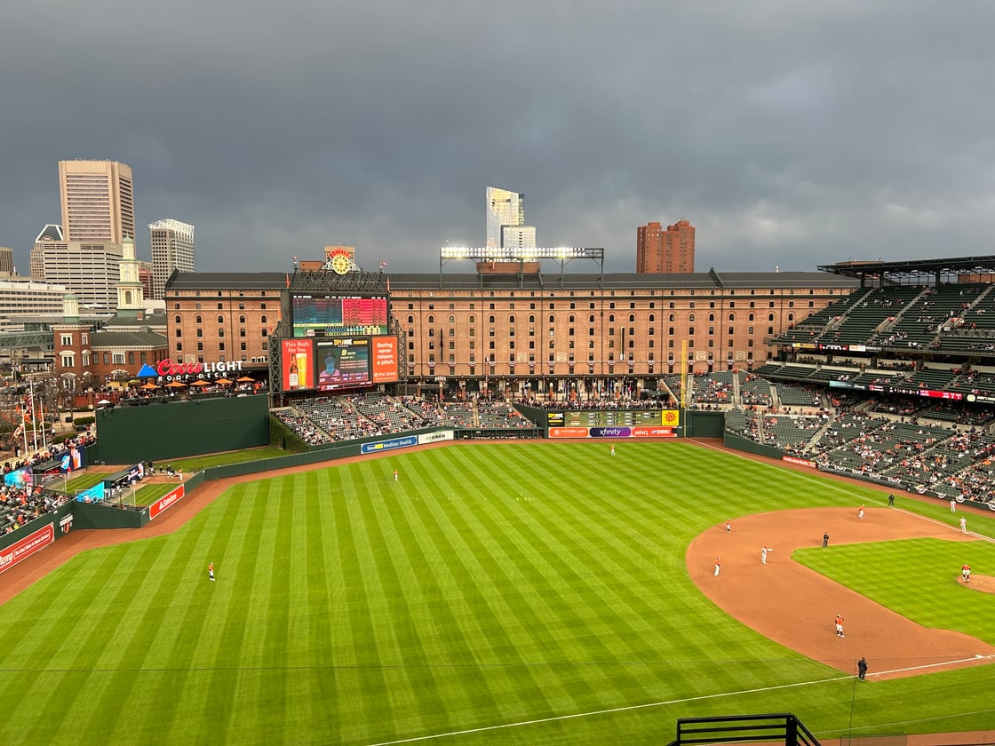 Camden Yards' green field with brown baseball diamond in front of brown building and green stands