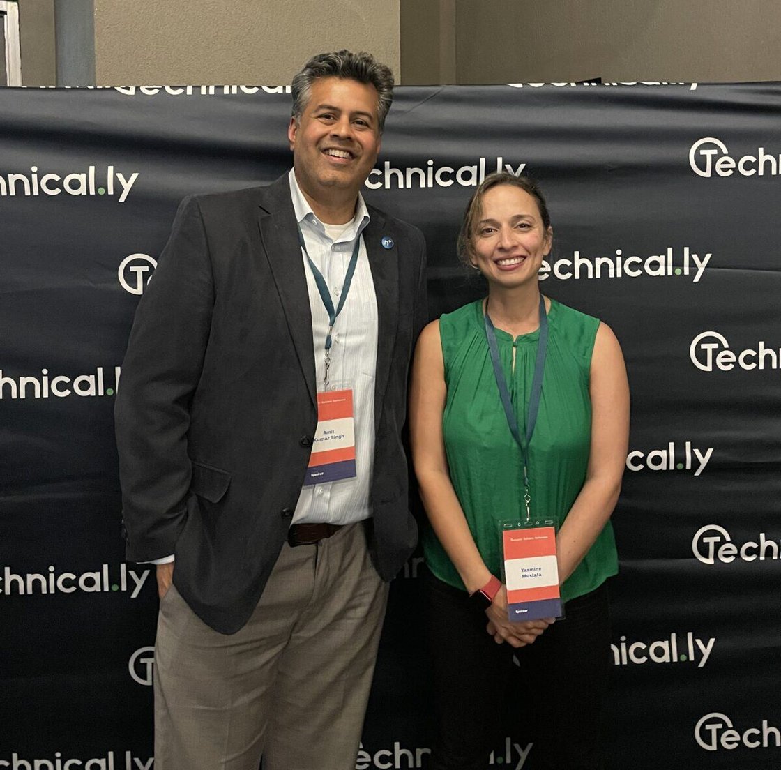 Man in grey blazer stands next to woman in green blouse in front of black backdrop with Technical.ly logos.